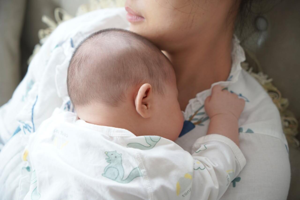 Postpartum mother sitting quietly while holding her newborn, looking thoughtful and slightly anxious, representing hormonal shifts after birth.